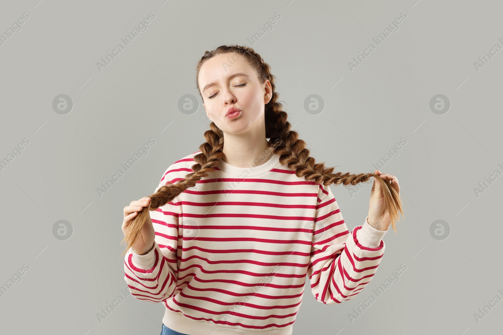 Photo of Woman with braided hair sending air kiss on grey background