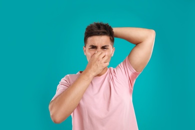 Young man with sweat stain on his clothes against blue background. Using deodorant