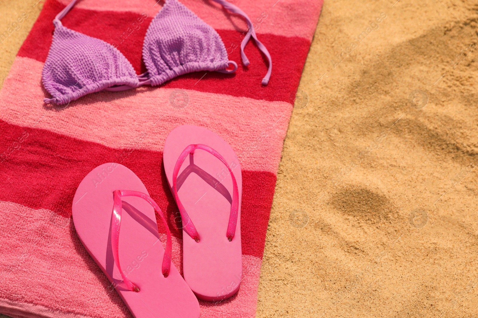 Photo of Beach towel with slippers and swimsuit on sand, space for text
