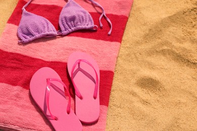 Photo of Beach towel with slippers and swimsuit on sand, space for text