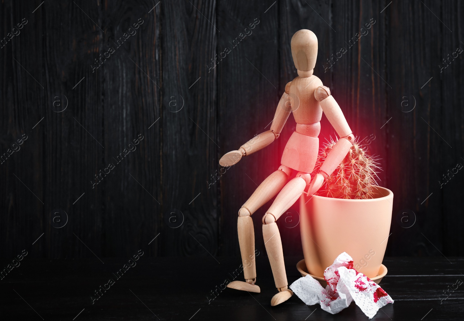 Image of Hemorrhoid concept. Wooden human figure, cactus and sheet of toilet paper with blood on black table, space for text