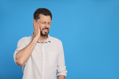 Photo of Man suffering from ear pain on light blue background, space for text
