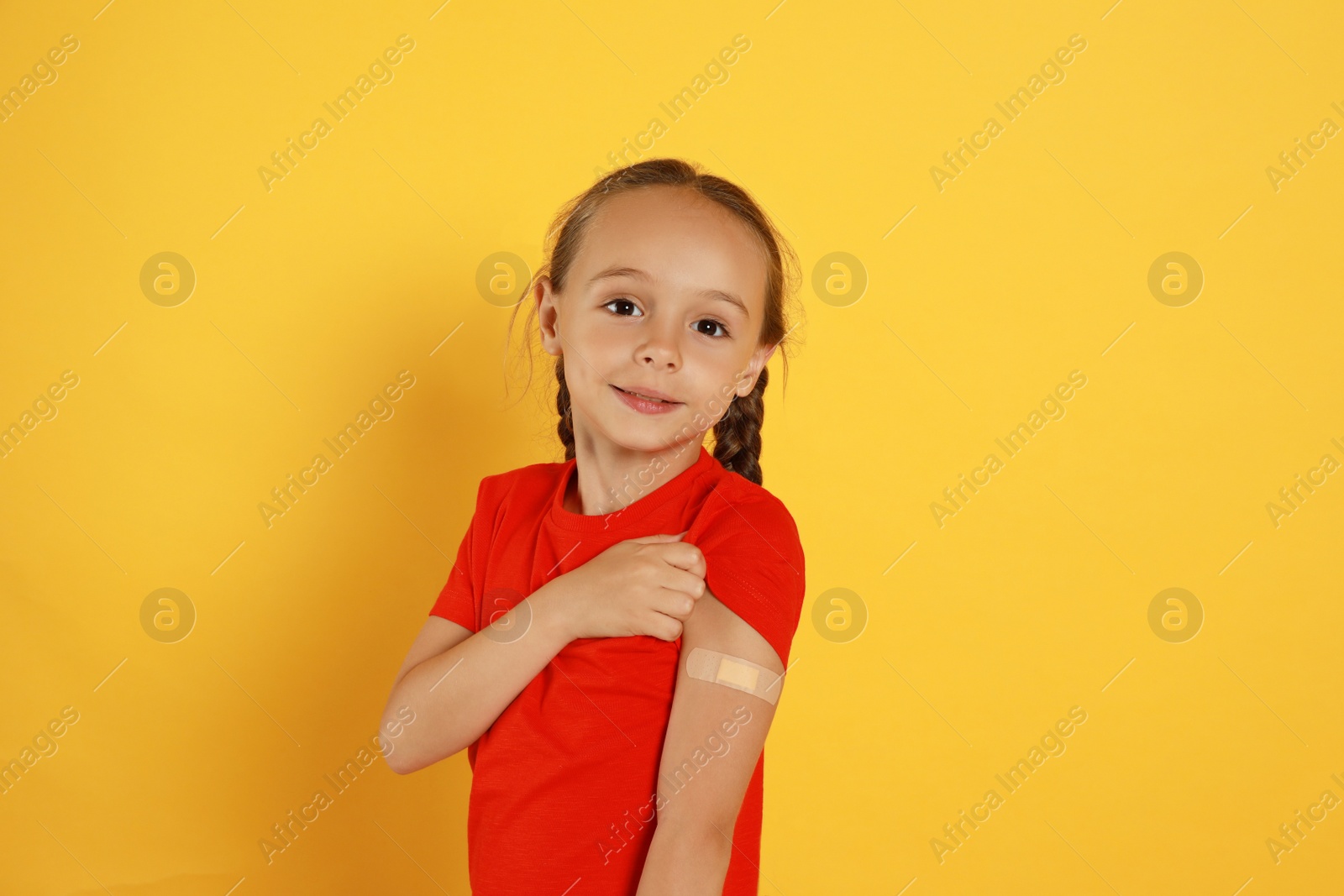 Photo of Vaccinated little girl showing medical plaster on her arm against yellow background