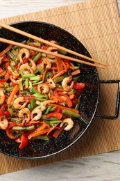 Photo of Shrimp stir fry with vegetables in wok and chopsticks on wooden table, top view