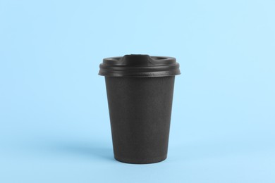 Black paper cup with plastic lid on light blue background. Coffee to go