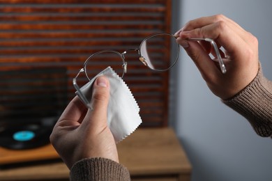 Photo of Man wiping glasses with microfiber cloth indoors, closeup