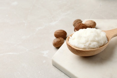 Shea butter in wooden spoon and nuts on table. Space for text