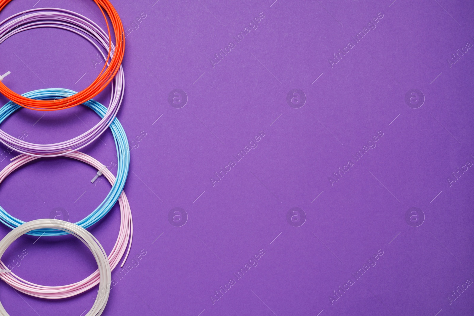 Photo of Colorful plastic filaments for 3D pen on violet background, flat lay. Space for text