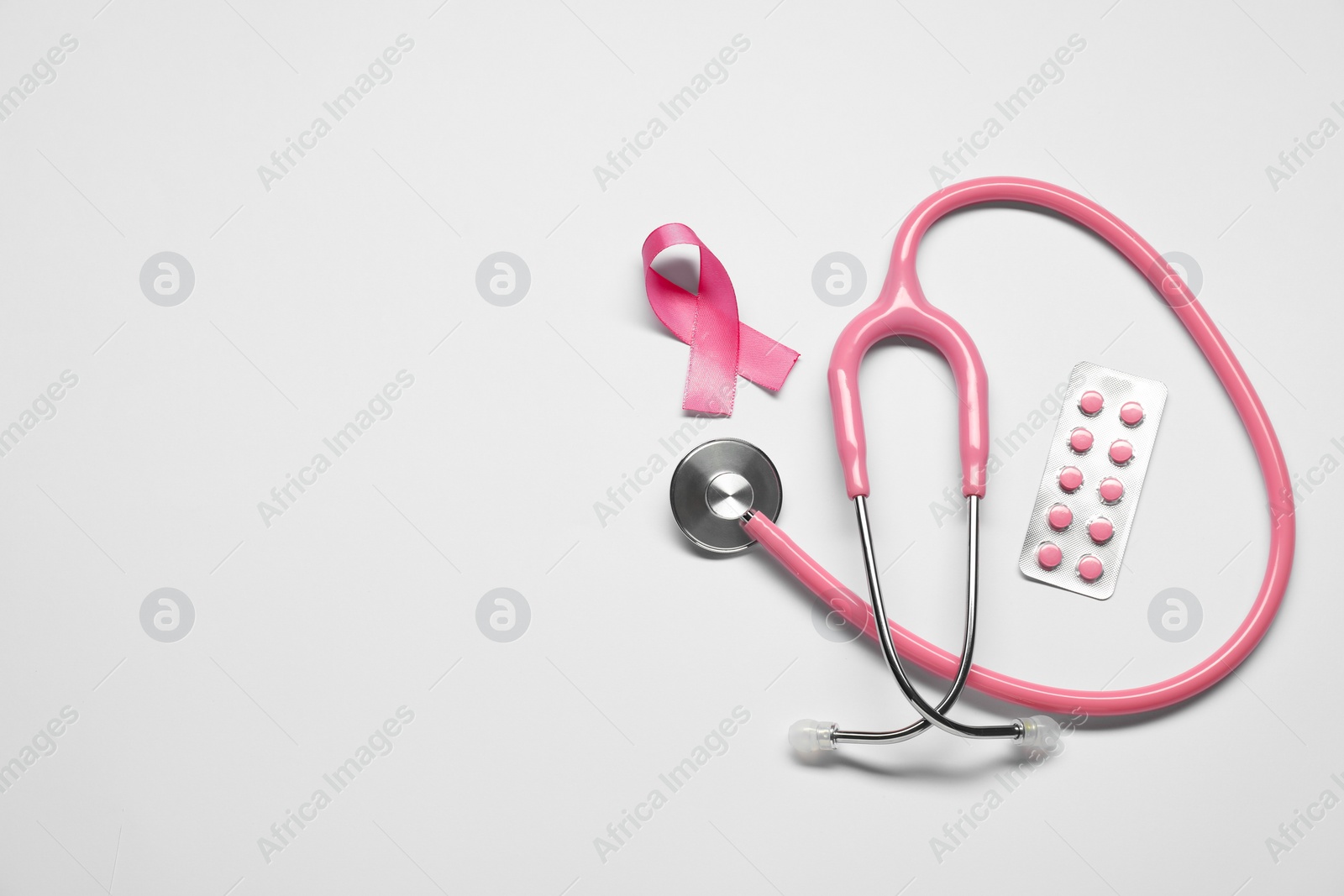 Photo of Breast cancer awareness. Pink ribbon, stethoscope and pills on white background, flat lay. Space for text