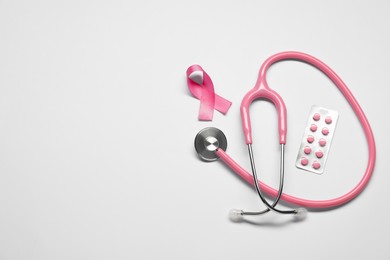 Breast cancer awareness. Pink ribbon, stethoscope and pills on white background, flat lay. Space for text