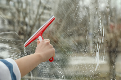 Woman cleaning window with squeegee at home, closeup. Space for text