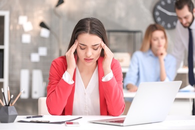 Photo of Young woman suffering from headache in office