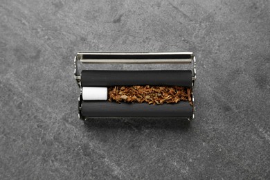 Photo of Cigarette roller with tobacco and filter on grey table, top view