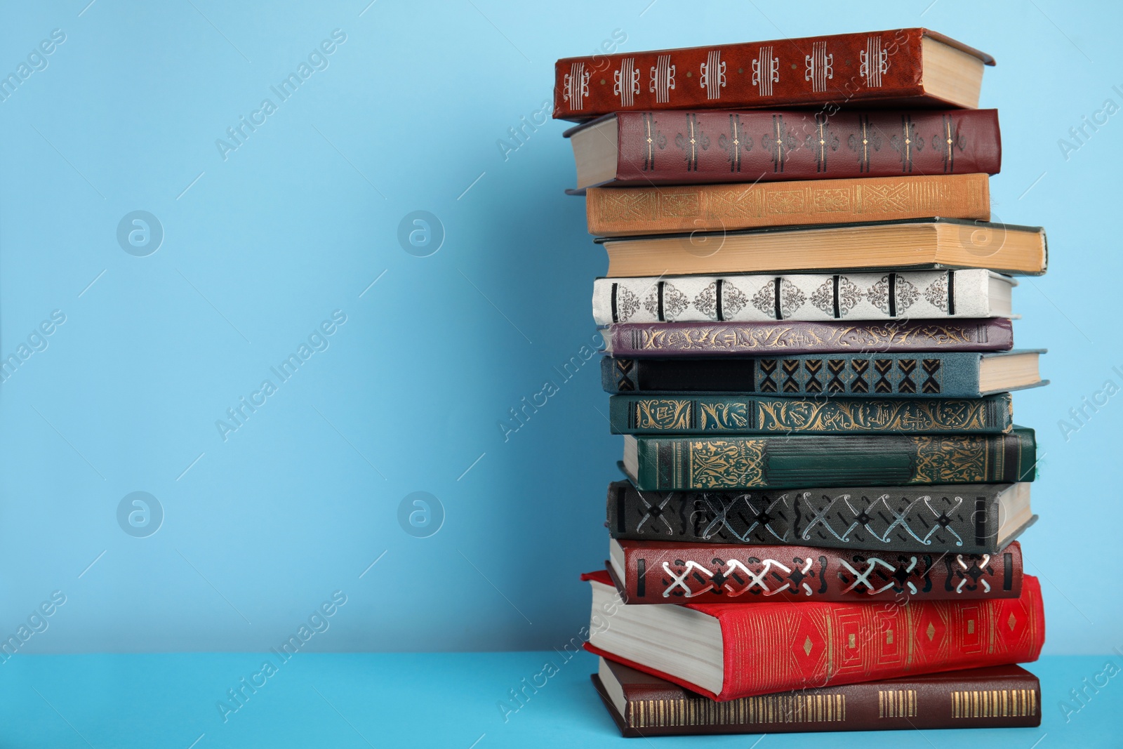 Photo of Stack of hardcover books on light blue background, space for text