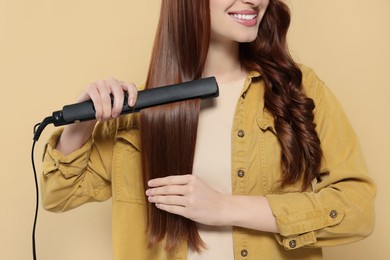 Photo of Young woman using hair iron on beige background, closeup