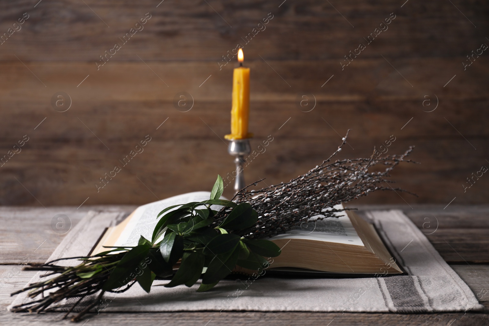 Photo of Bible, willow branches and burning candle on table, closeup