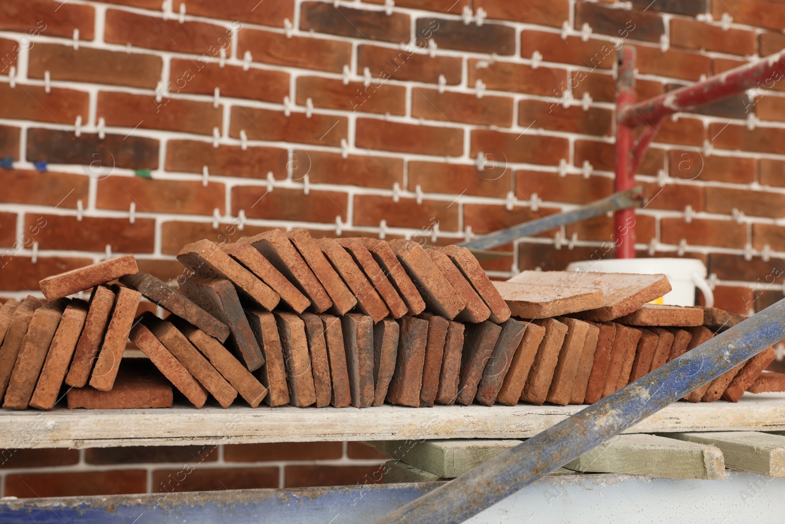 Photo of Many decorative bricks on scaffolding near wall. Tiles installation process