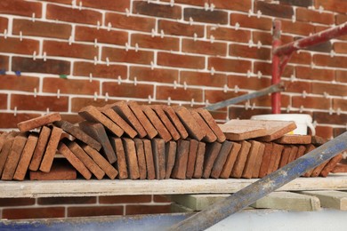Photo of Many decorative bricks on scaffolding near wall. Tiles installation process