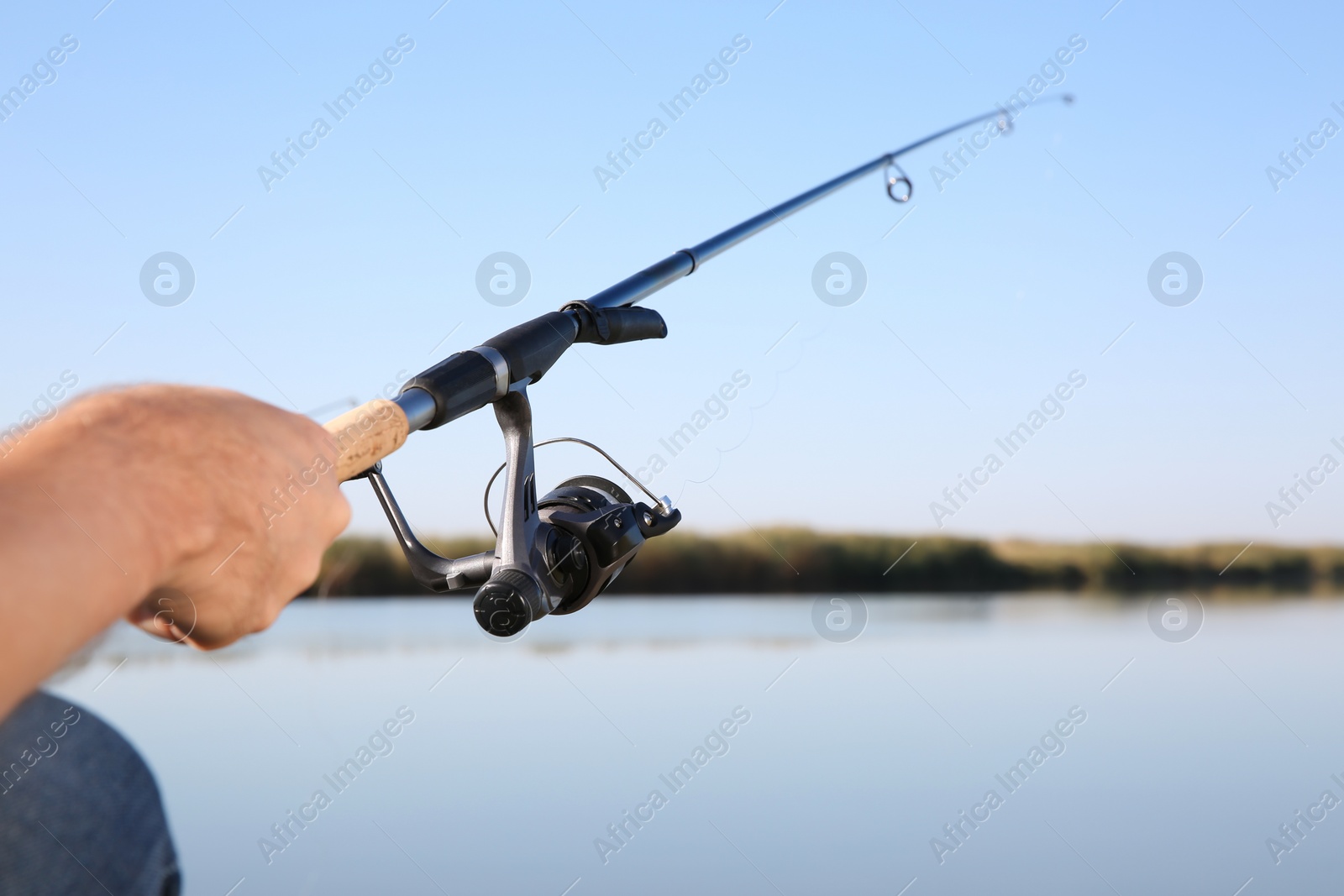 Photo of Man fishing alone at riverside on sunny day, closeup