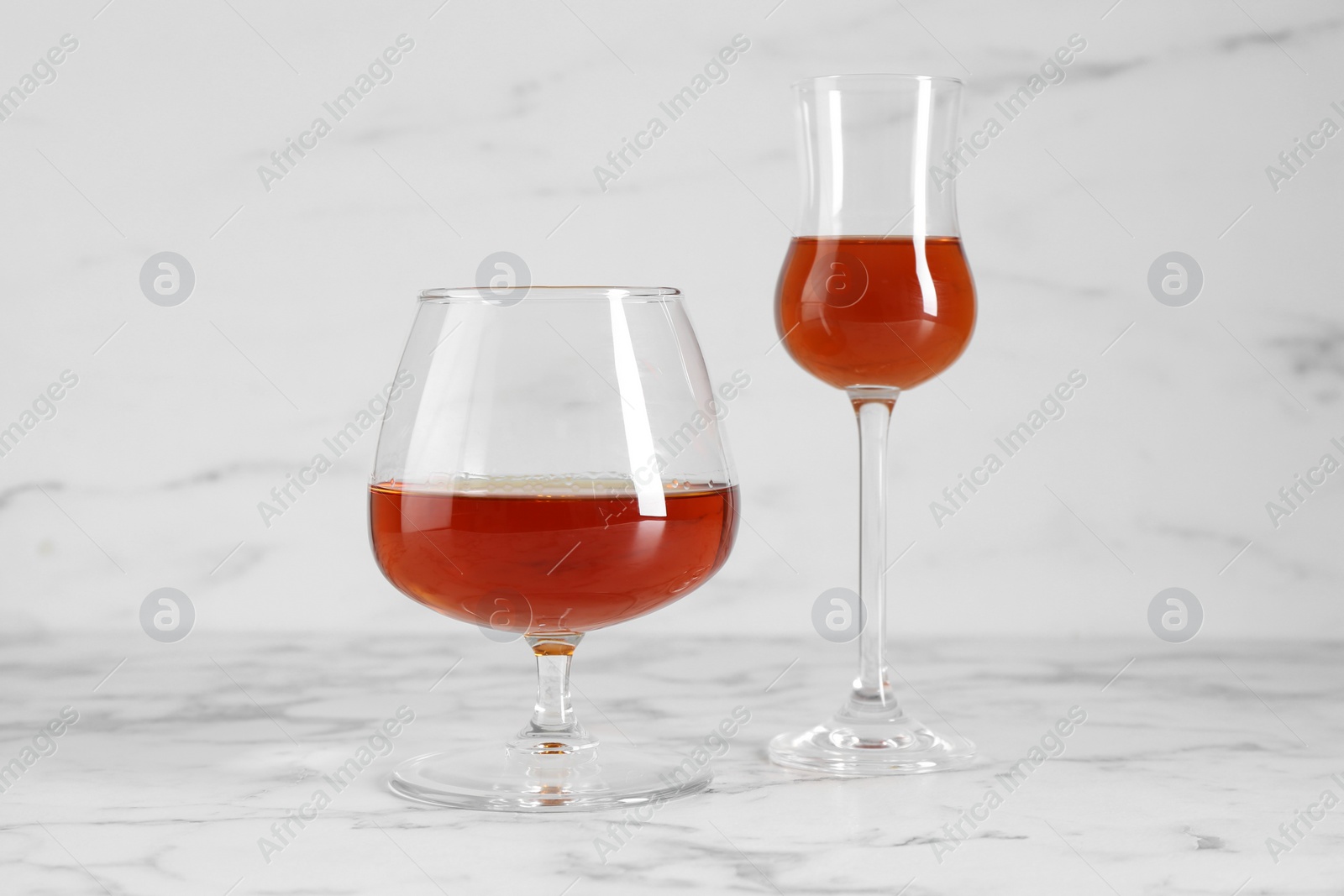 Photo of Delicious liqueurs in glasses on white marble table