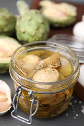 Photo of Jar of delicious artichokes pickled in olive oil on grey table, closeup