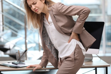 Young woman suffering from back pain in office