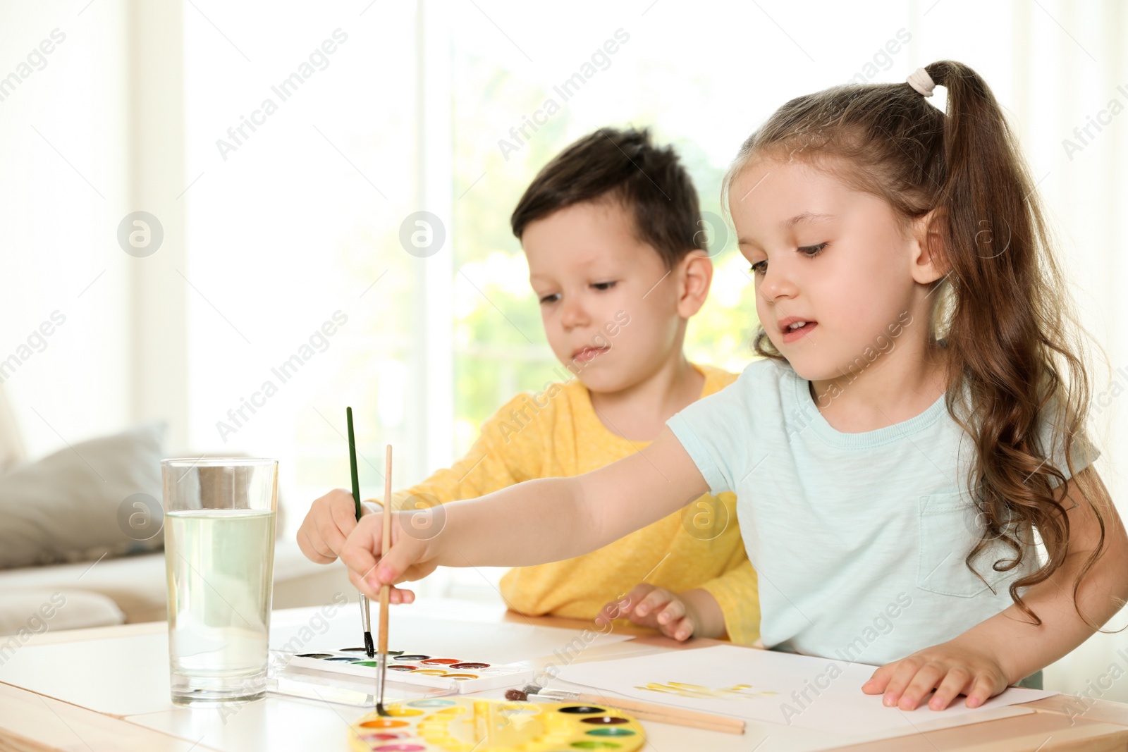 Photo of Cute little boy and girl drawing at table in living room