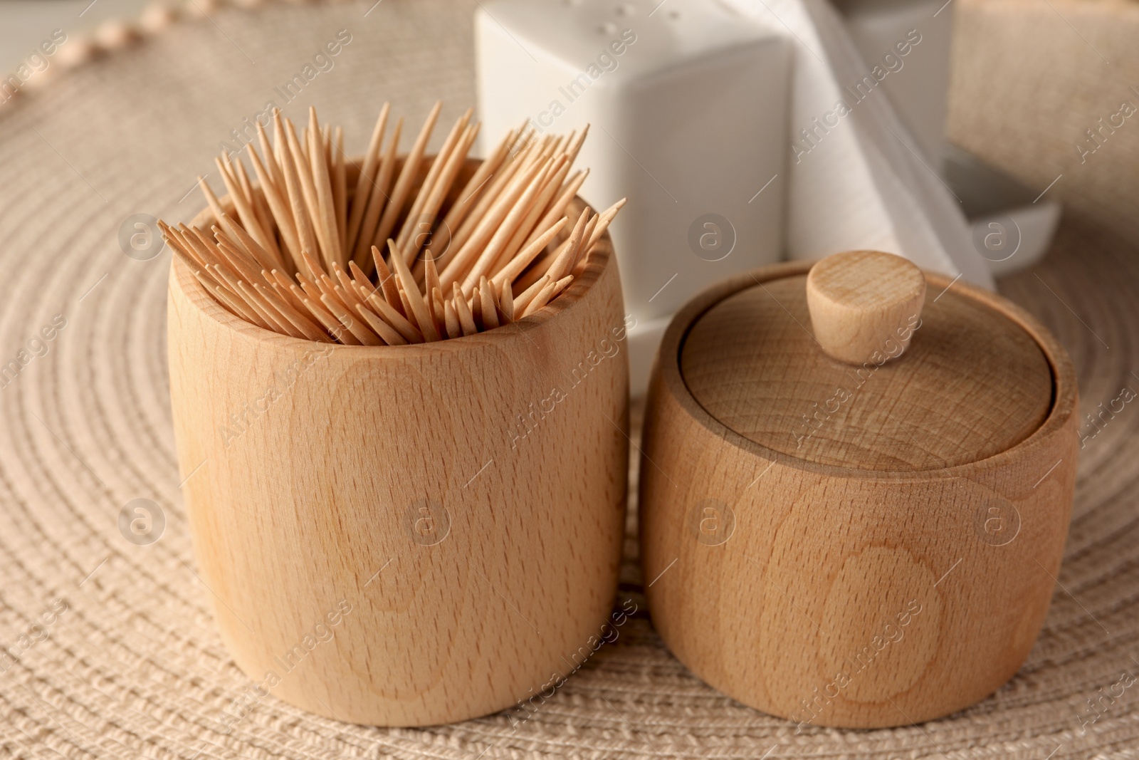 Photo of Wooden holder with many toothpicks on wicker mat, closeup