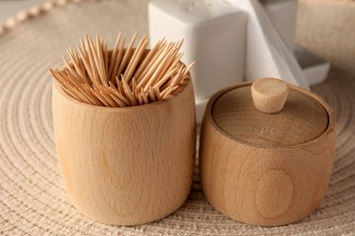 Photo of Wooden holder with many toothpicks on wicker mat, closeup