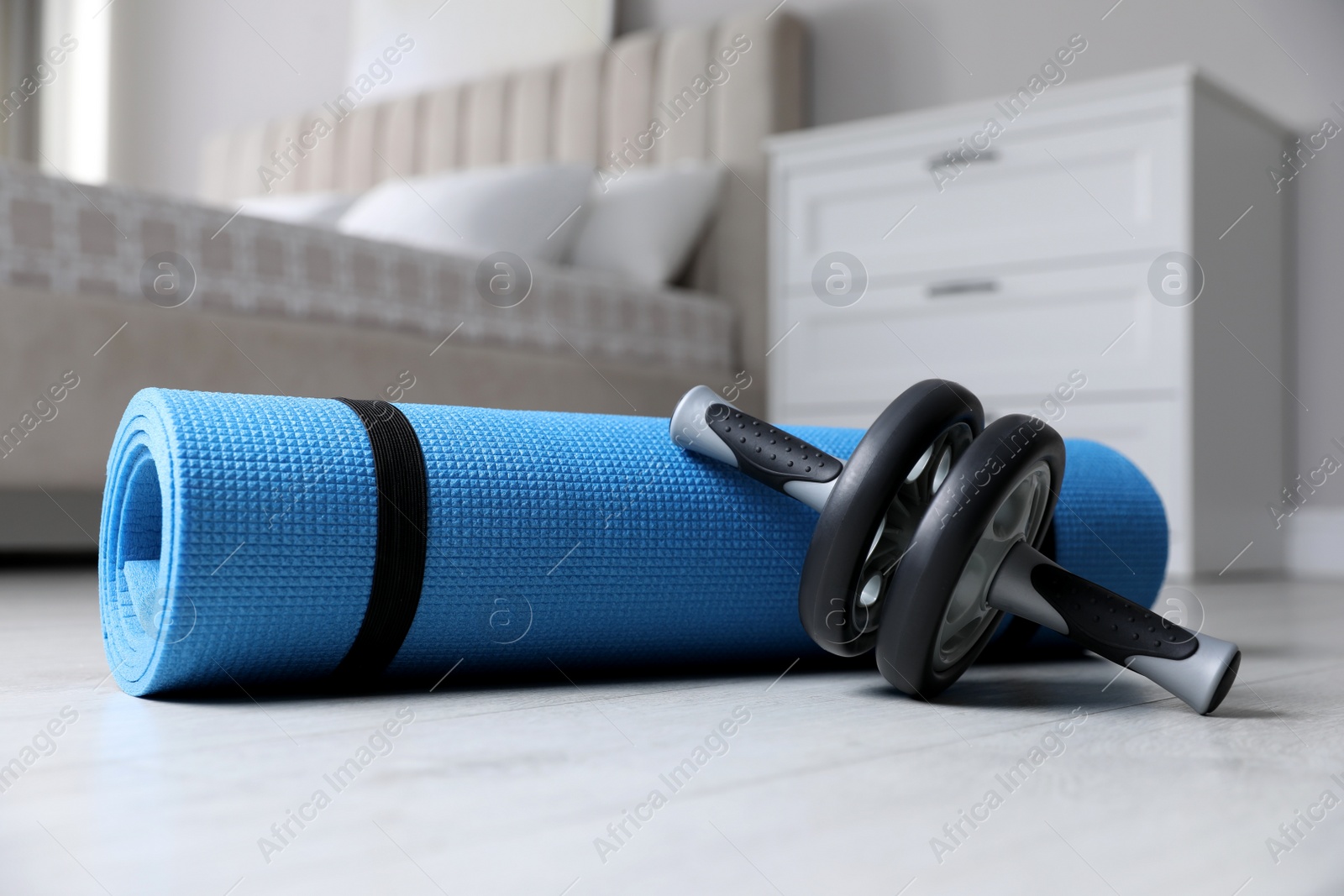 Photo of Abs roller and yoga mat on floor indoors. Fitness at home