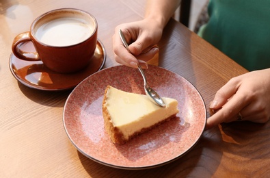 Photo of Woman eating slice of cheesecake at table, closeup