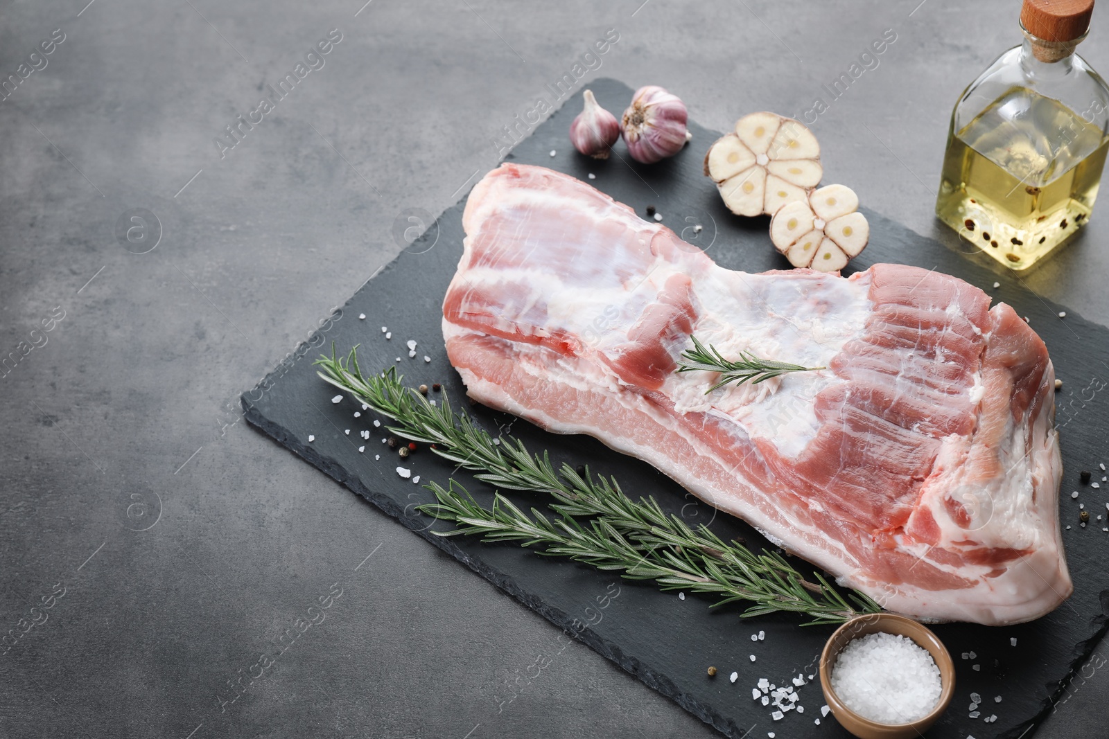 Photo of Piece of raw pork belly, rosemary, garlic and salt on grey textured table, above view. Space for text