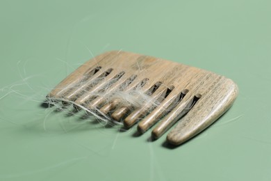 Photo of Comb with lost hair on green background, closeup