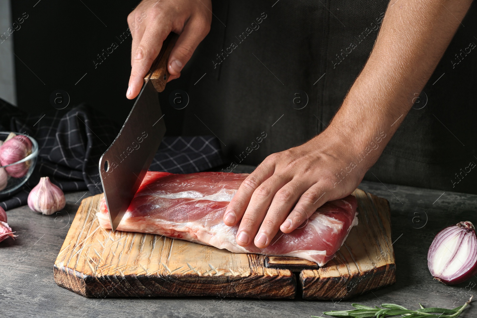 Photo of Man cutting fresh raw meat on table against dark background, closeup