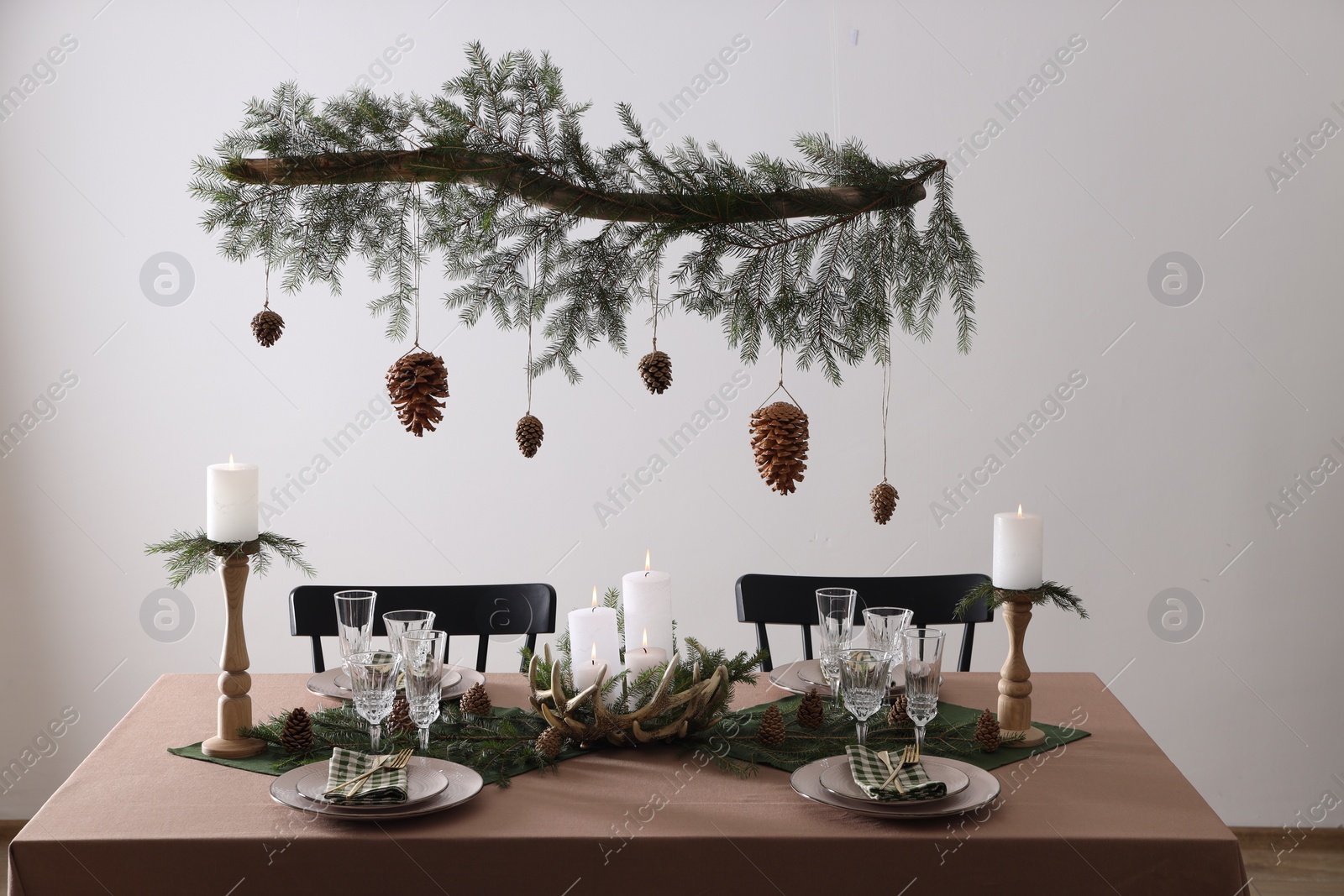 Photo of Christmas celebration. Cones hanging from fir tree branch over table with burning candles and tableware