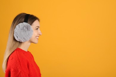 Happy woman wearing warm earmuffs on yellow background, space for text