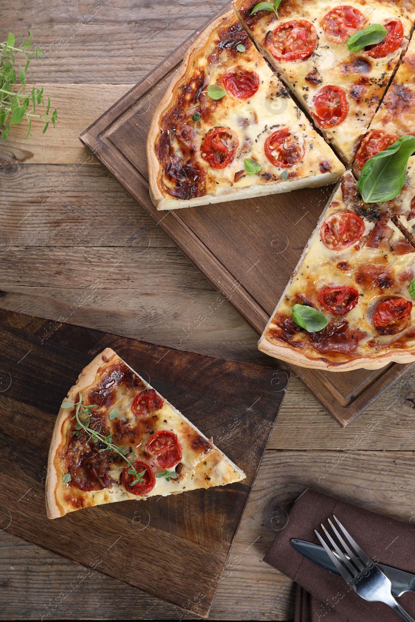 Photo of Cut delicious homemade quiche with prosciutto, tomatoes and basil on wooden table, flat lay