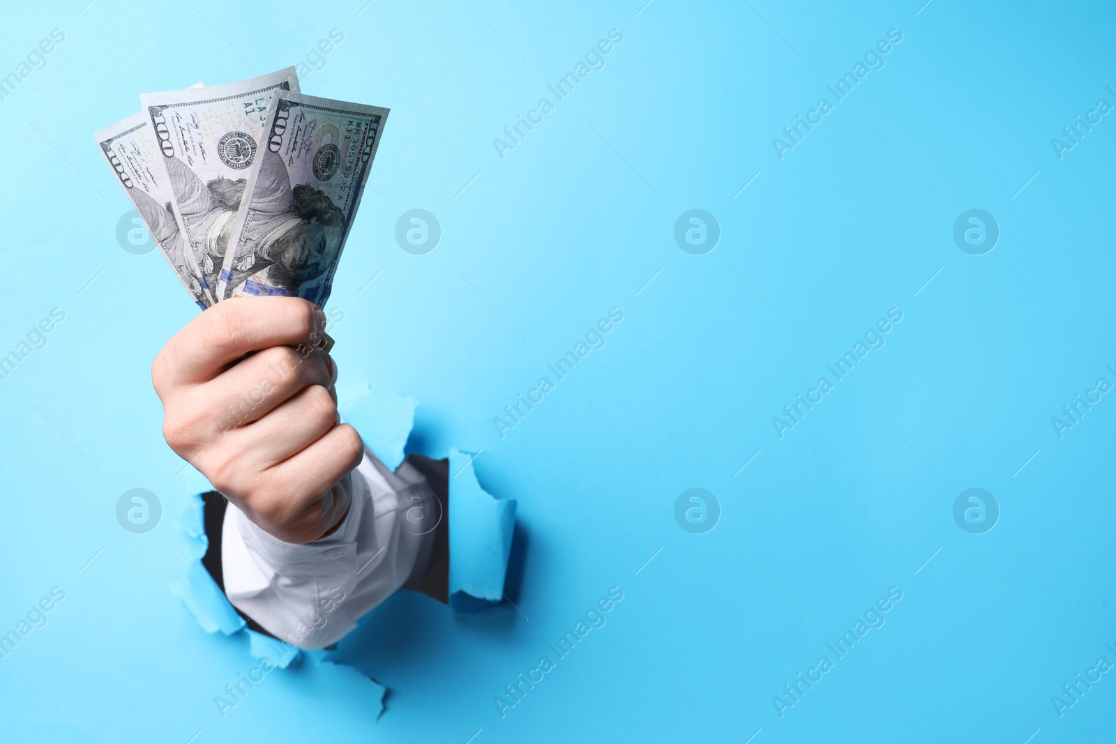 Photo of Businessman breaking through light blue paper with money in fist, closeup. Space for text