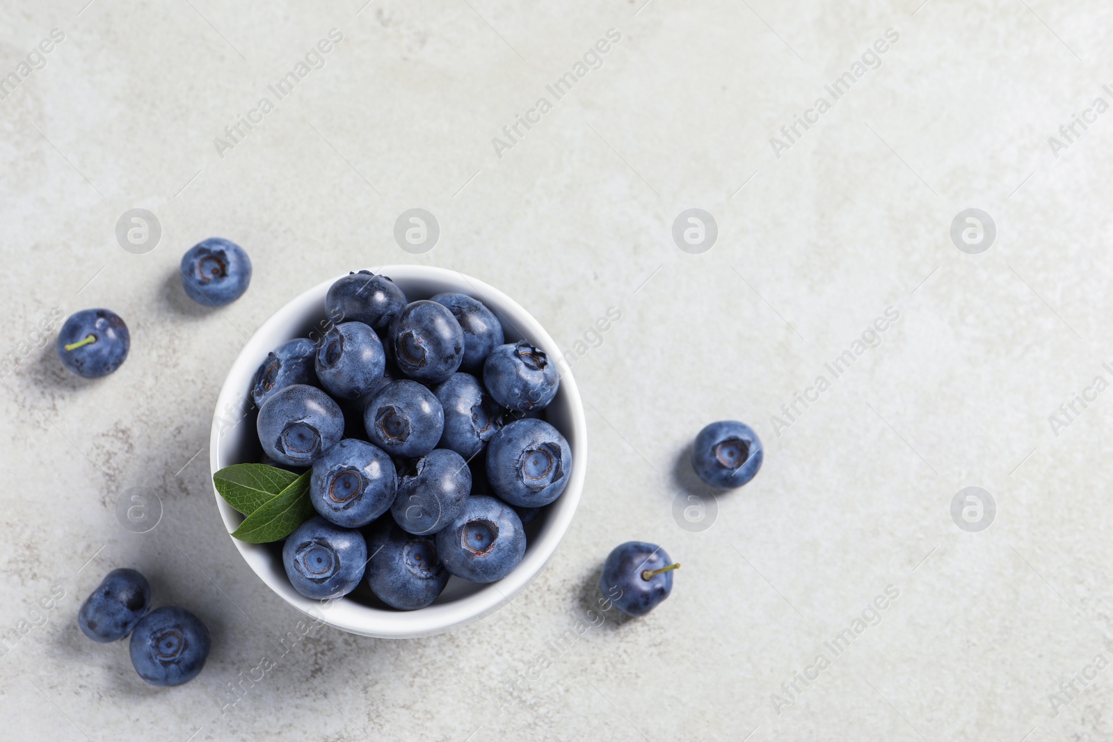 Photo of Bowl of fresh tasty blueberries on light grey table, flat lay. Space for text