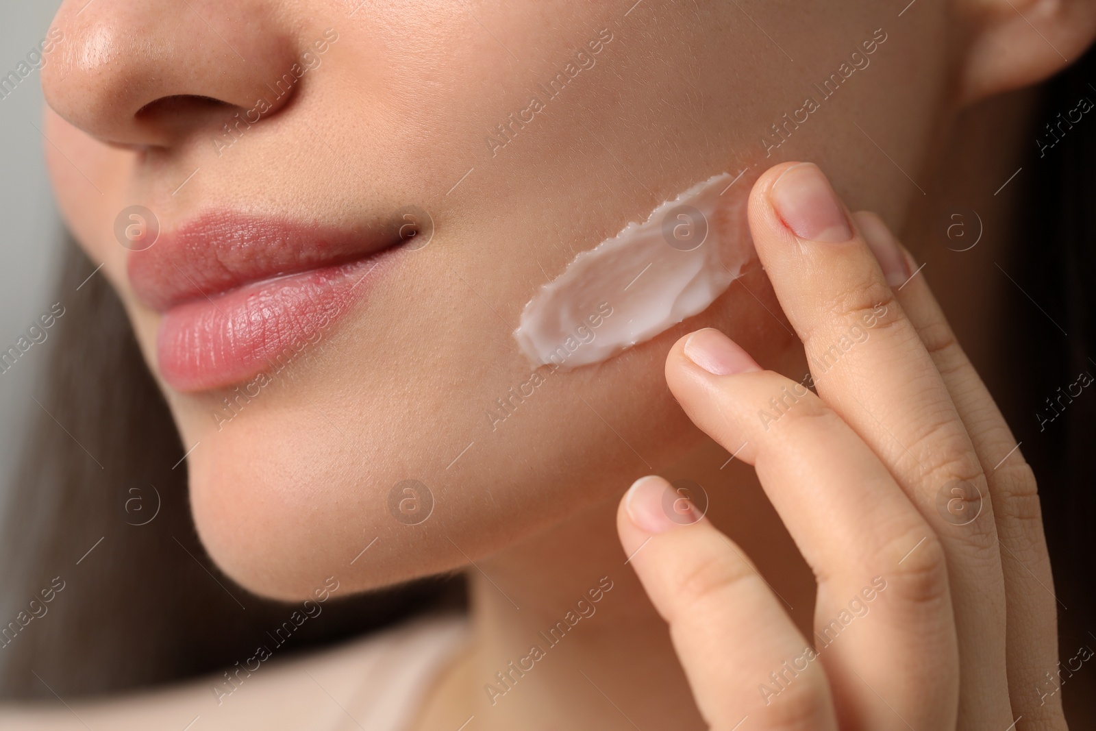 Photo of Young woman with dry skin applying cream onto her face, closeup