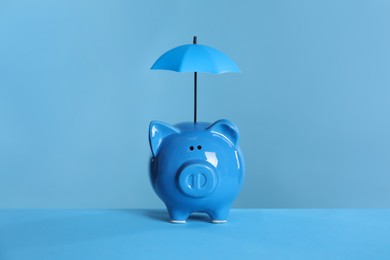 Photo of Small umbrella and piggy bank on light blue background