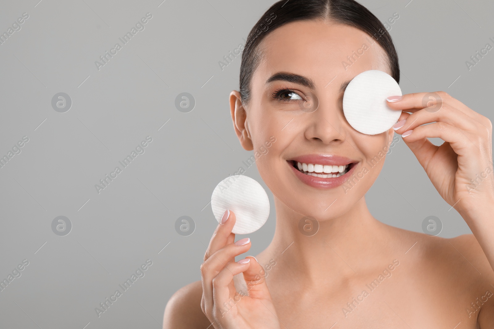 Photo of Beautiful woman removing makeup with cotton pads on light grey background. Space for text