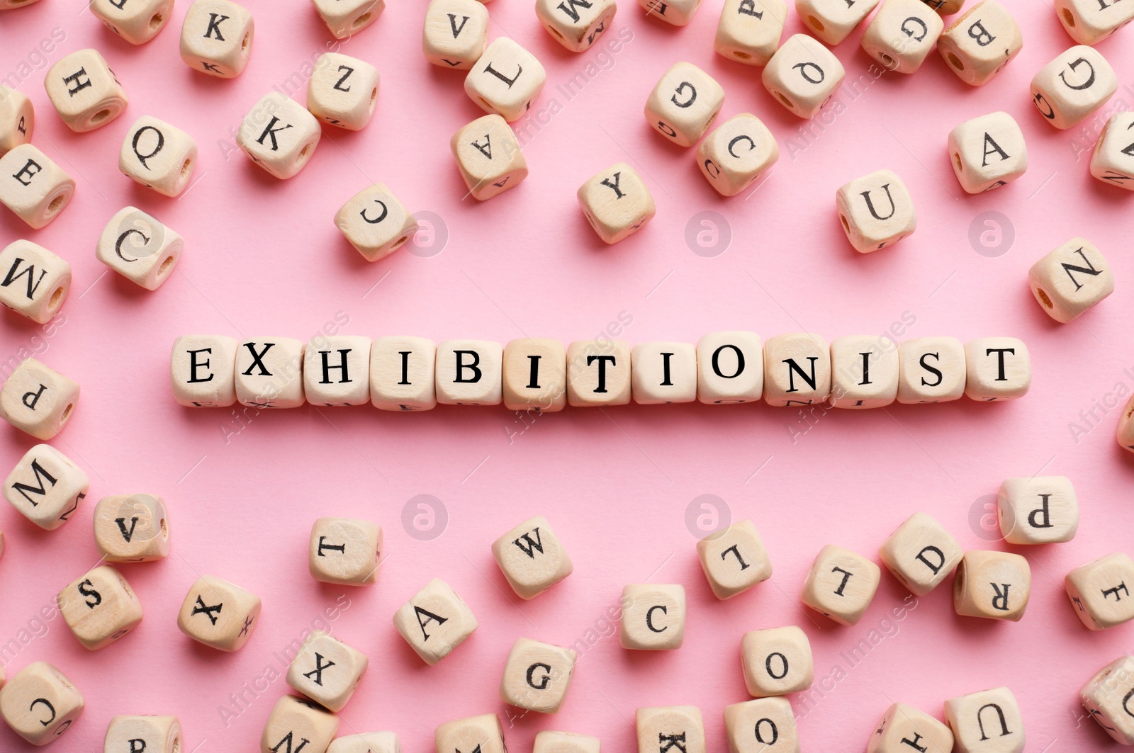 Photo of Word EXHIBITIONIST made with wooden cubes on pink background, flat lay