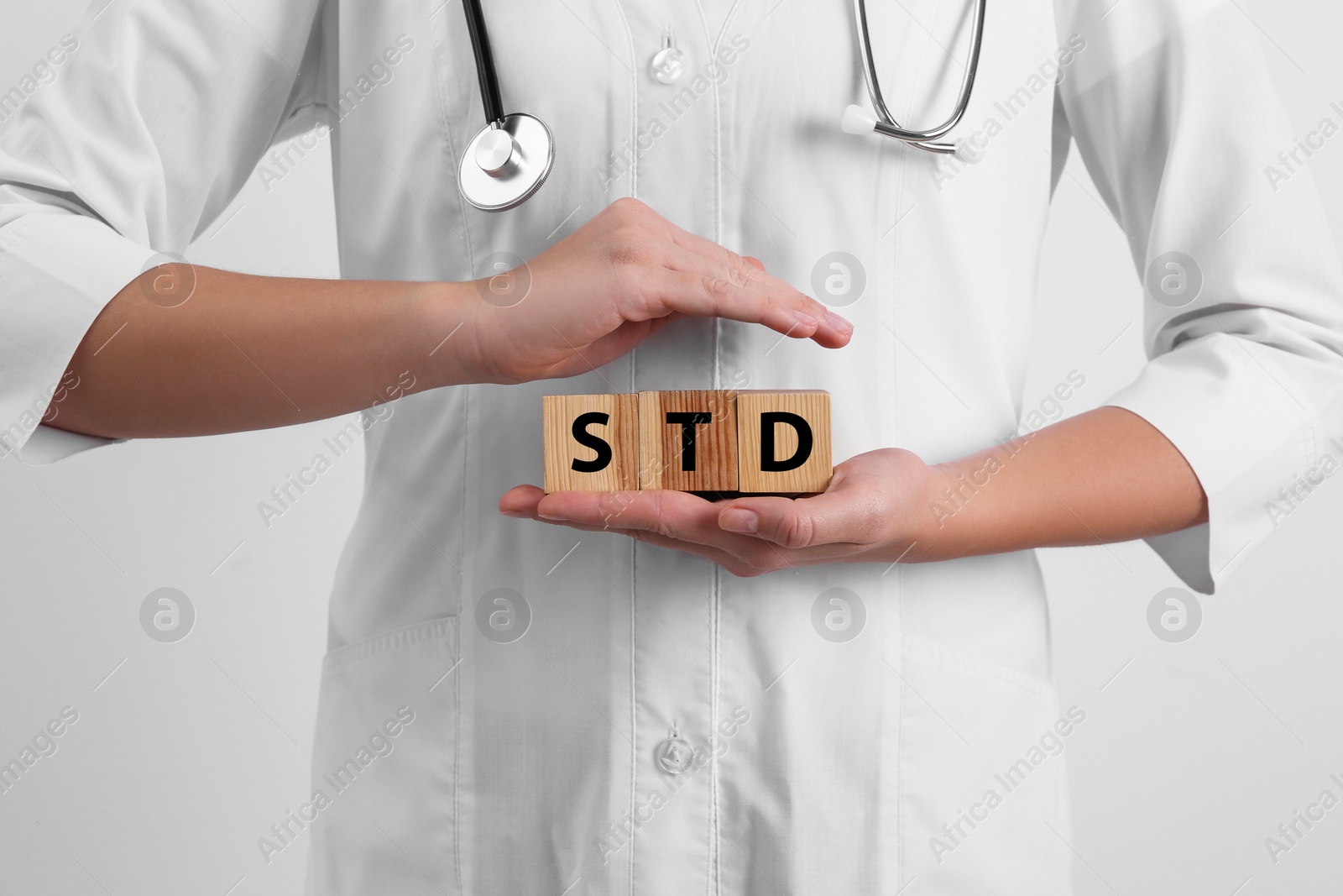 Photo of Doctor holding wooden cubes with abbreviation STD on white background, closeup