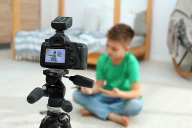Photo of Cute little blogger with selfie stick recording video at home, focus on camera