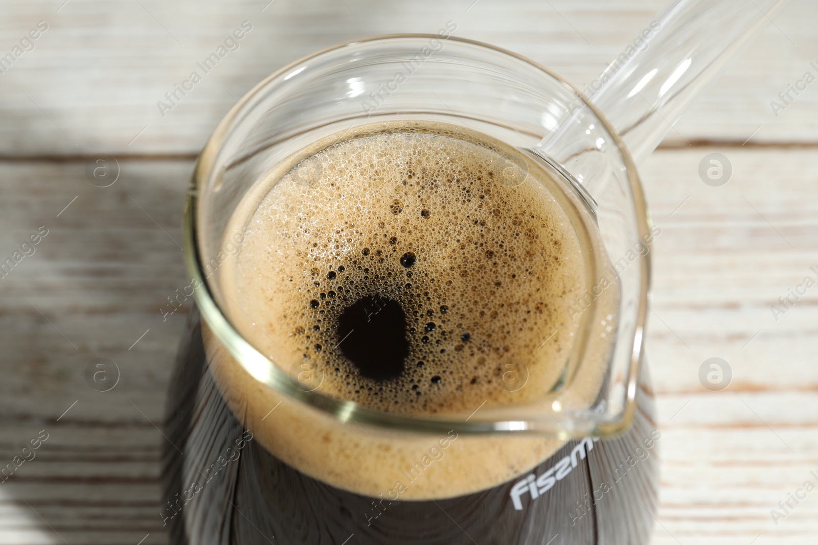 Photo of Glass turkish coffee pot with hot drink on wooden table, closeup