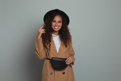 Beautiful African American woman with stylish waist bag on grey background