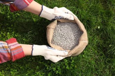 Photo of Woman with bag of fertilizer on green grass outdoors, top view