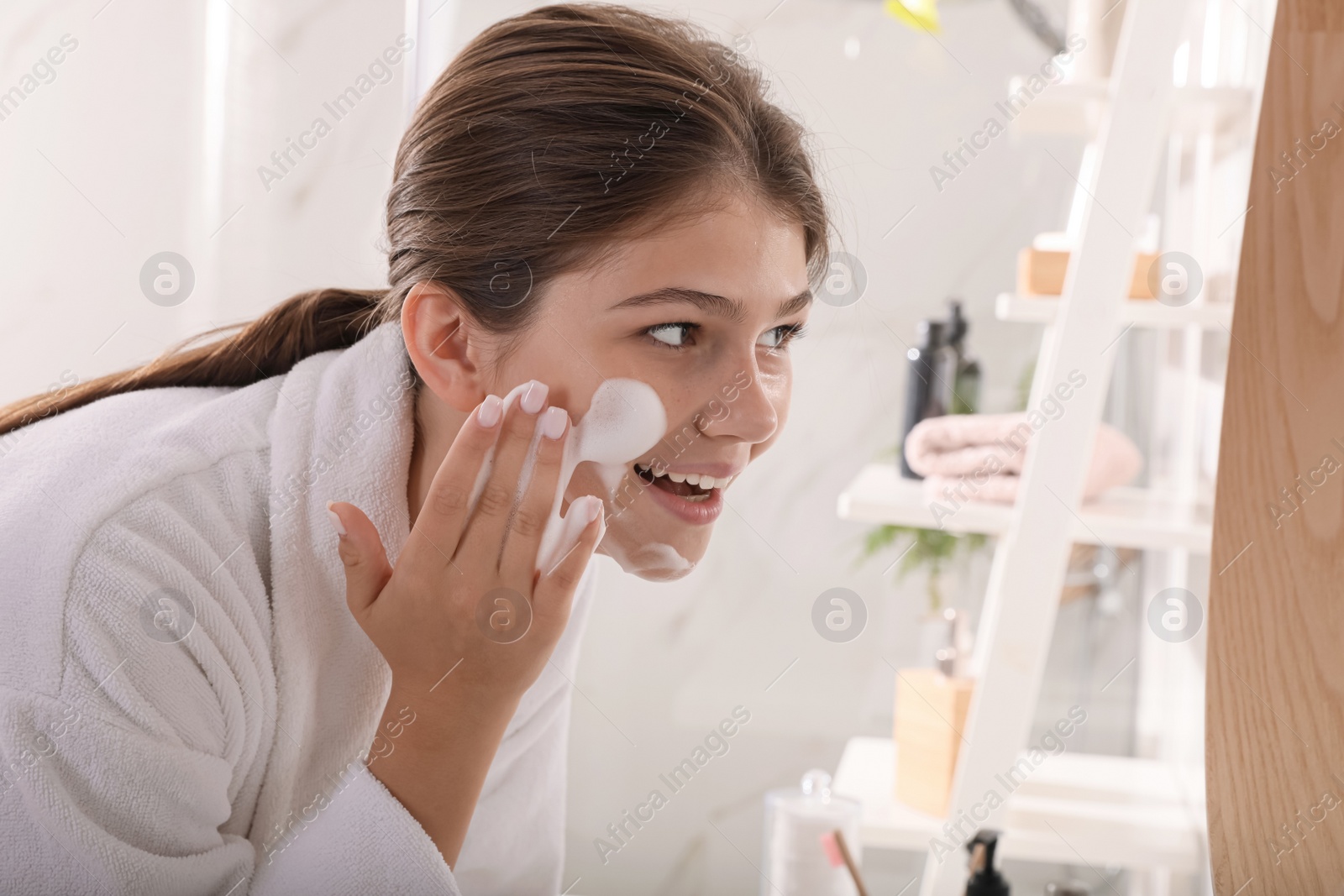 Photo of Beautiful teenage girl applying cleansing foam onto face in bathroom. Skin care cosmetic