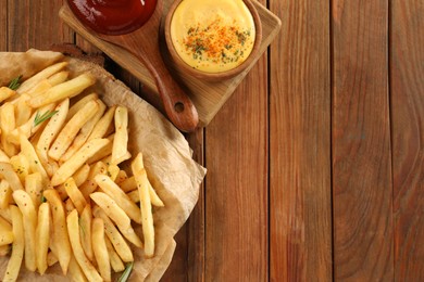 Delicious french fries served with sauces on wooden table, flat lay. Space for text